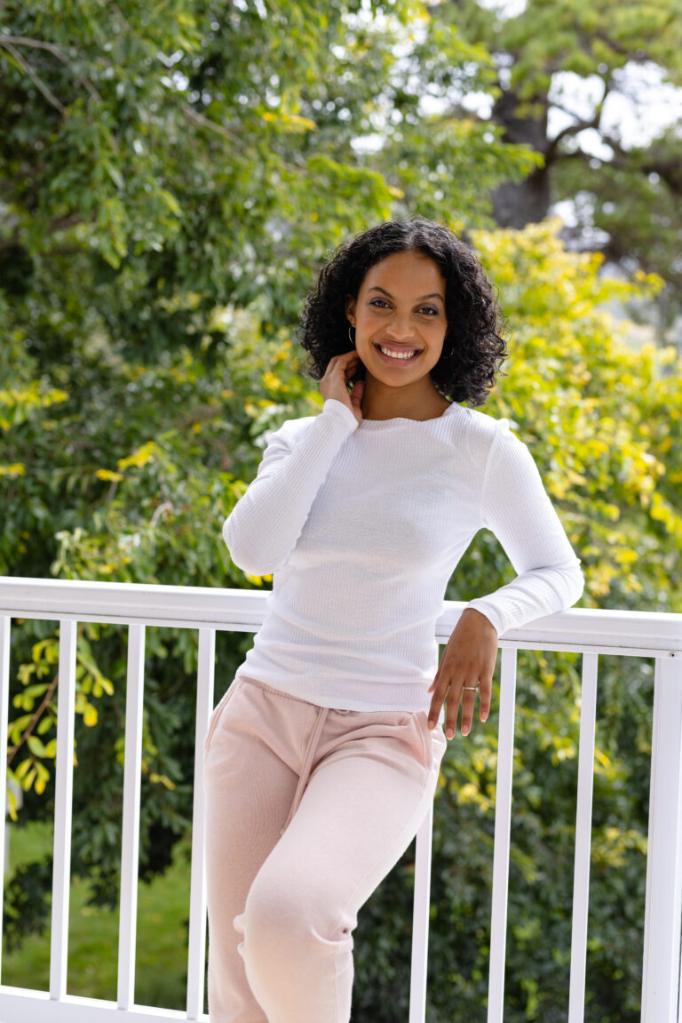 Happy biracial woman in slippers relaxing on balcony at home with treetops in background. Wellbeing, domestic life and lifestyle, unaltered.