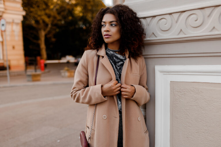 Outdoor fashion portrait of glamour sensual young stylish black  lady wearing trendy fall outfit  , grey velvet  sweater and beige wool coat. Co
