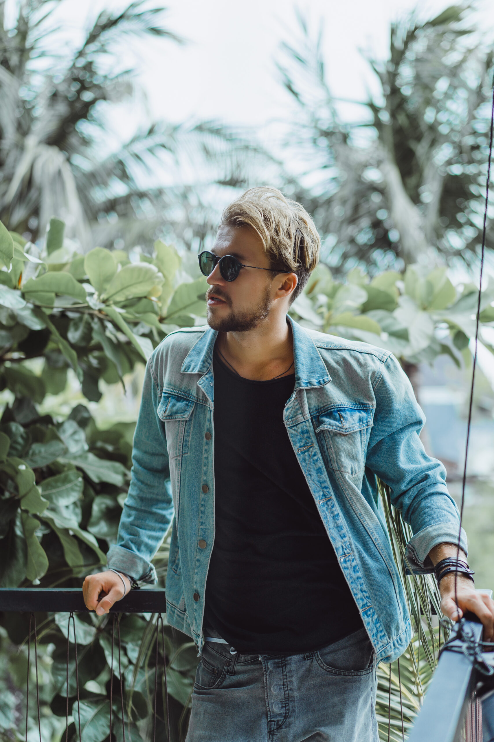 young attractive man posing in a tropical location, on a background of palm trees and greenery, in sunglasses